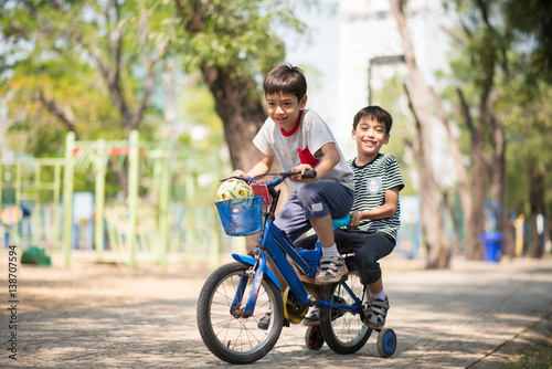 Little sibling boy riding bike together in the park