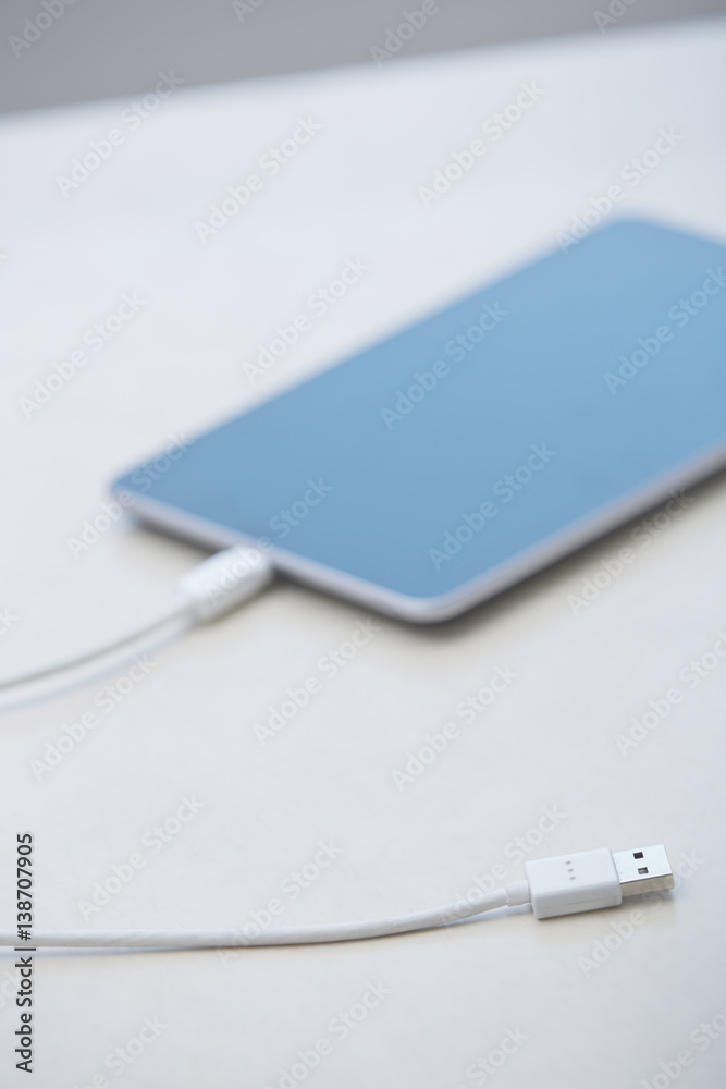 Fototapeta premium Digital tablet with USB cable laying on a table