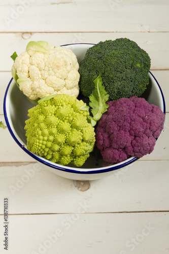 Fresh organic white and purple cauliflower, broccoli, romanesco. On wooden board, bowl, wooden cutting board.