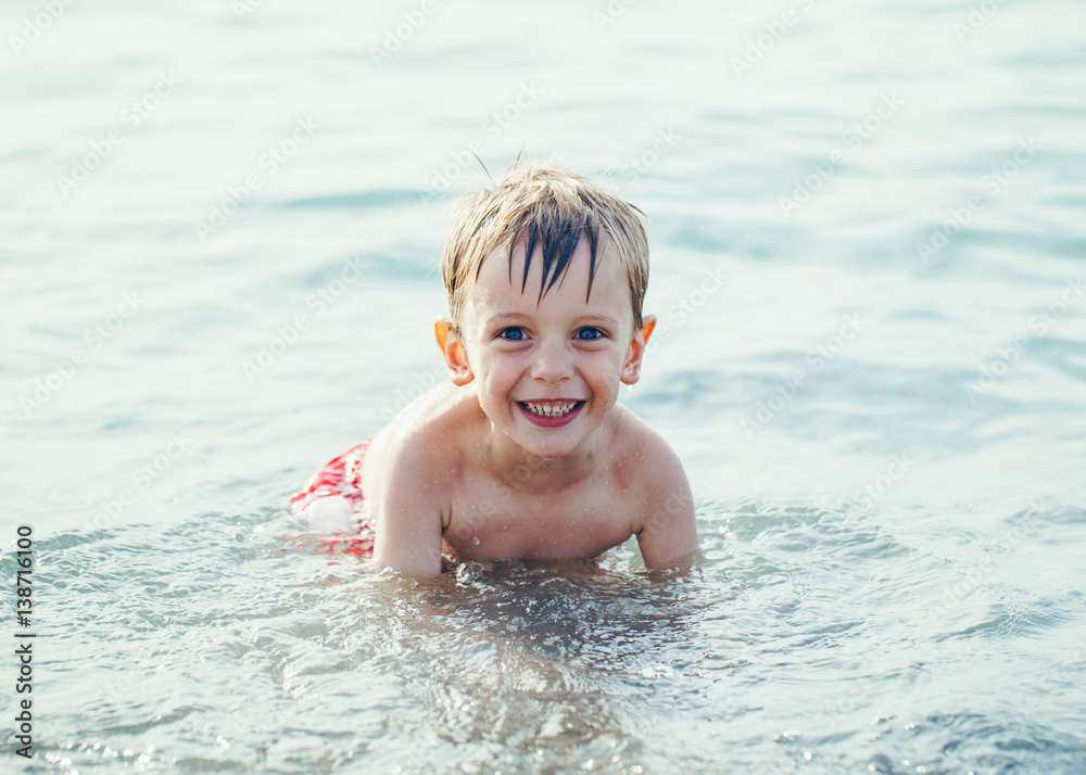 Portrait of funny adorable smiling laughing white Caucasian one young little boy in water ocean sea, emotional active healthy lifestyle summer mood