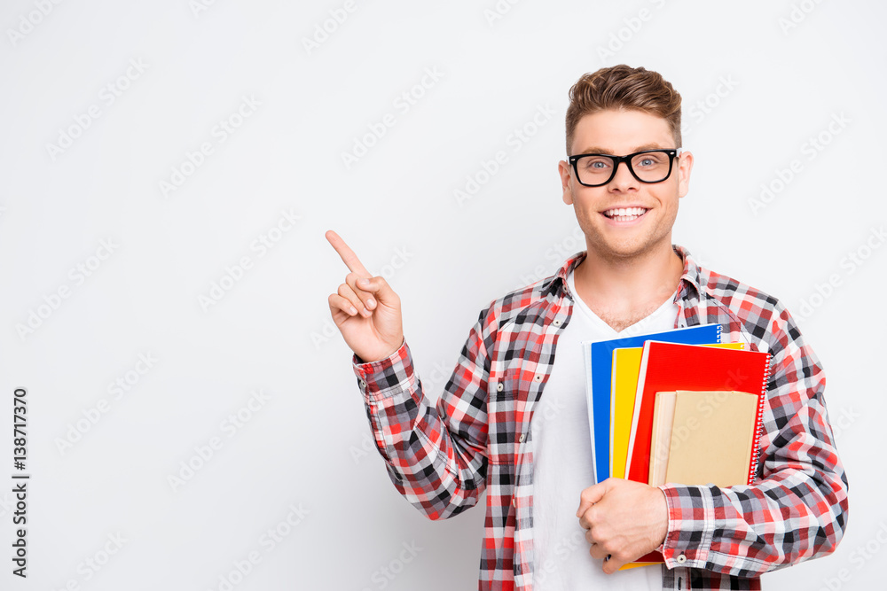 Cheerful student holding educational materials and pointing on a copy space Cheerful student holding educational materials and pointing on a copy space