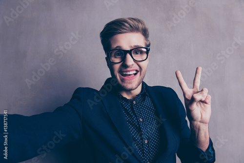 A young happy man taking selfie and showing two fingers up
