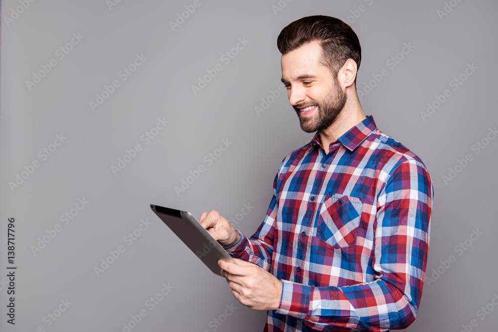 Smiling stylish man isolated on gray background holding his tablet and reading information Smiling stylish man isolated on gray background holding his tablet and reading information