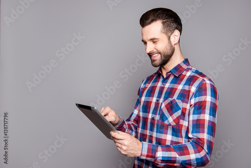 Smiling stylish man isolated on gray background holding his tablet and reading information