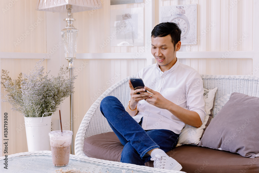 Obraz premium Asian man using a mobile phone and drink coffee in bakery shop
