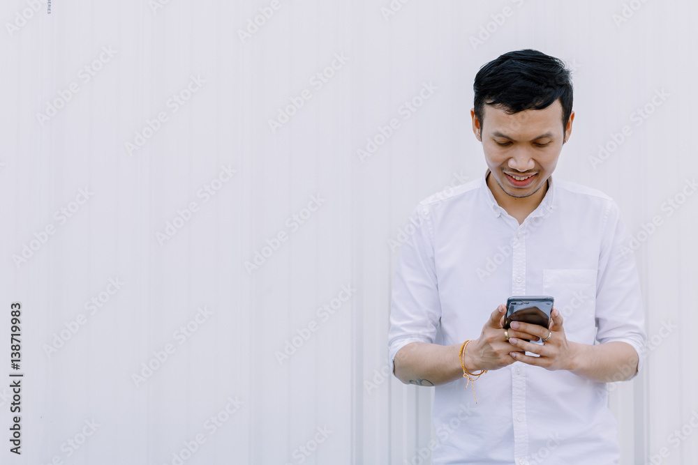 Asian man using a mobile phone smile with white walls Asian man using a mobile phone smile with white walls