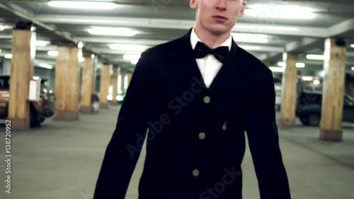 Wallpaper Mural Young blusinessman in a black suit with bow-tie walking on the parking with big leather bag. Slowmotion Torontodigital.ca