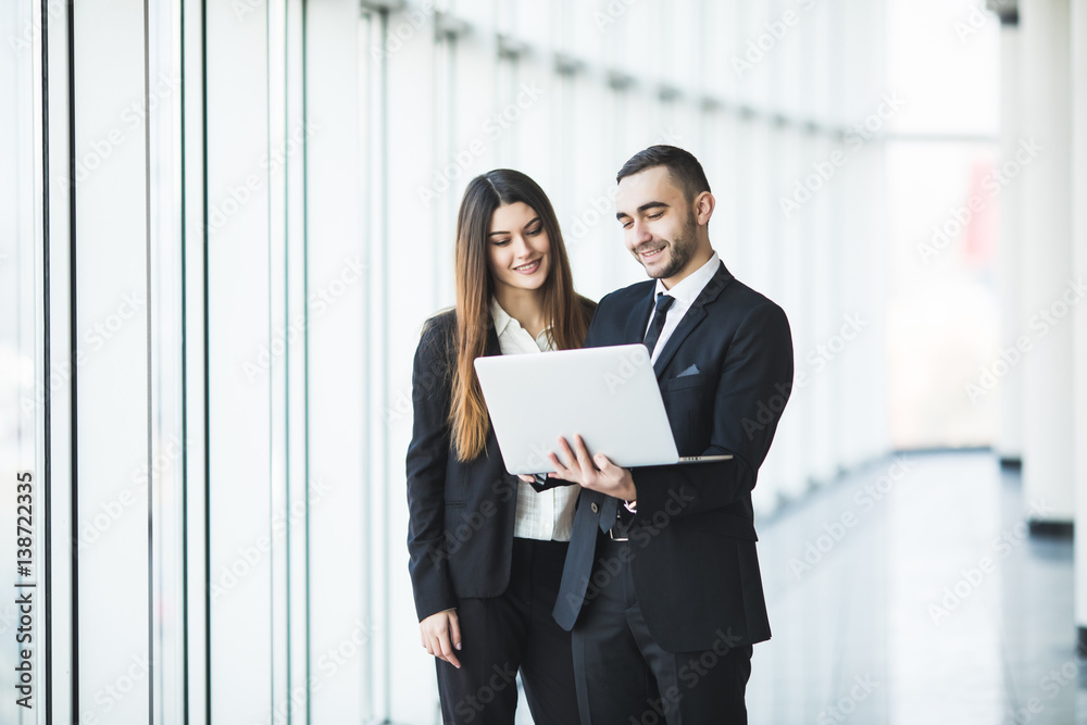 Couple discussing new project on the laptop atanding against in office room with panoramic windows Couple discussing new project on the laptop atanding against in office room with panoramic windows
