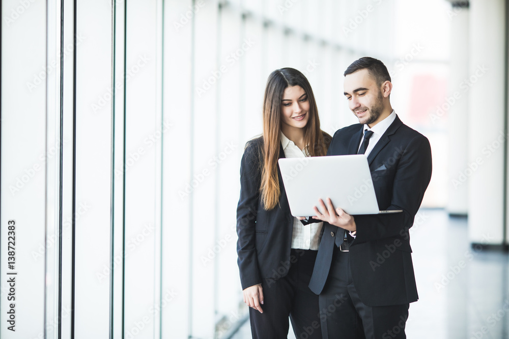 Couple discussing new project on the laptop atanding against in office room with panoramic windows Couple discussing new project on the laptop atanding against in office room with panoramic windows