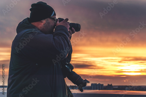 Photographer with two cameras taking a shot of sunset from roof 