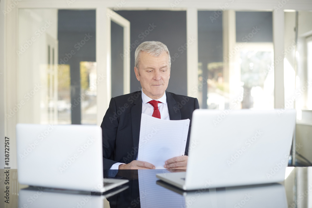 Financial businessman working online. Shot of a senior financial director sitting at desk and working on laptops in the office. 