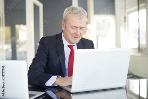 Financial businessman working online. Shot of a senior financial director sitting at desk and working on laptops in the office. 