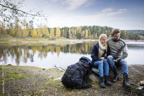 Couple With Backpack Relaxing On Lakeshore During Camping