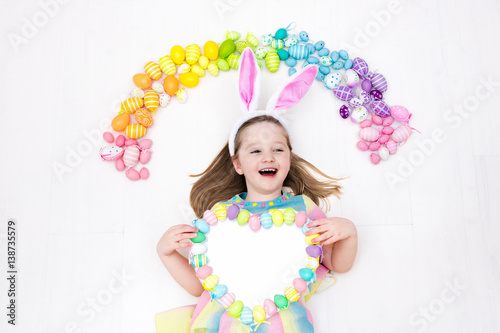 Child on Easter egg hunt. Pastel rainbow eggs.