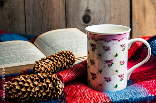 cup of hot tea with lemon on wool shawl with opened book, burning candle, cones and lavender