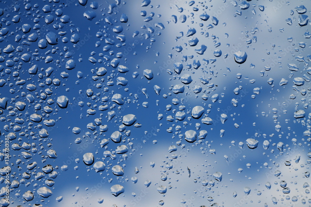 Rain drops on window with blue cloudy sky in background , spring rainy day 