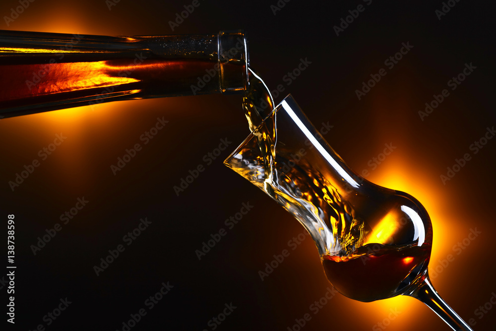 Pouring alcohol into a glass on dark background
