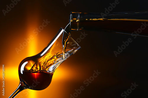 Fototapeta Pouring alcohol into a glass on dark background
