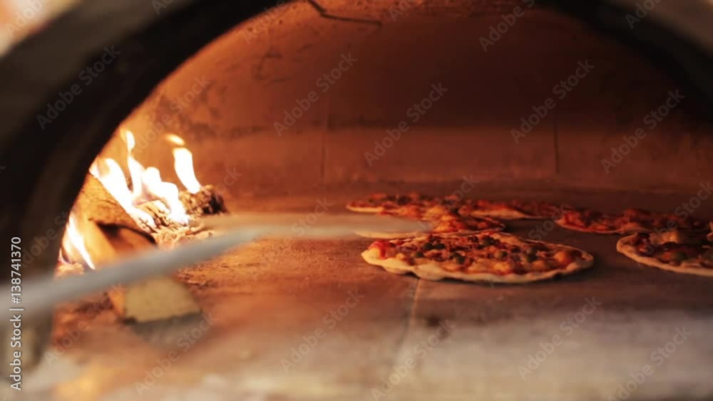 peel placing pizza baking in oven at pizzeria