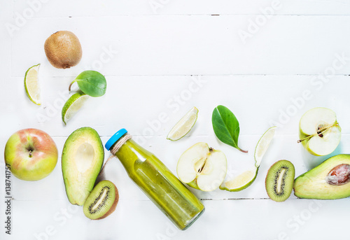 Green smoothie in bottl with avocado, apple and kiwi on white wooden background. photo