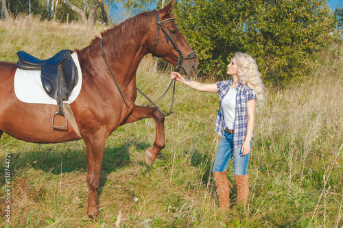 Beautiful blonde girl taking care of the horse at the ranch