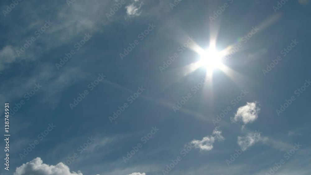 Sun shining bright on blue sky day with minimal clouds and vapor trail passing by.