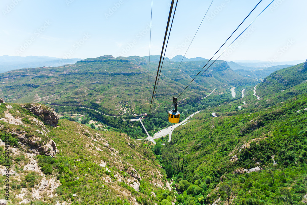 Panoramic views of the valley from the mountains of Montserrat. Near Barcelona, Spain. Beautiful nature in shades of green on a background of blue sky. Yellow cablecar cabin, cableway Panoramic views of the valley from the mountains of Montserrat. Near Barcelona, Spain. Beautiful nature in shades of green on a background of blue sky. Yellow cablecar cabin, cableway