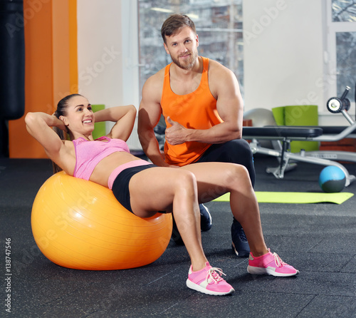 Young woman doing exercise with trainer in gym