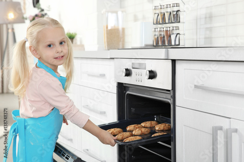 Little girl taking biscuits from oven
