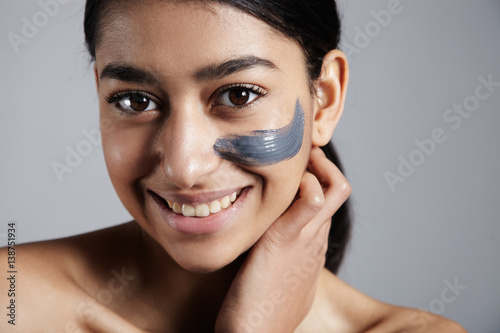 mixed race woman with clay coal grey facial cleansing mask treatment.  photo