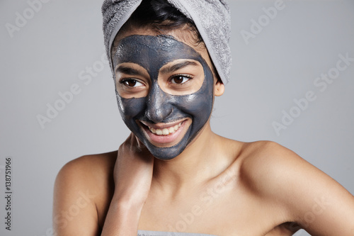 mixed race woman with clay coal grey facial cleansing mask treatment. 