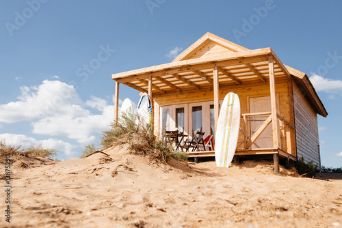 Holiday house on the beach. Wooden house with boards for wind serfing on a sand beach. Summer vacation concept.