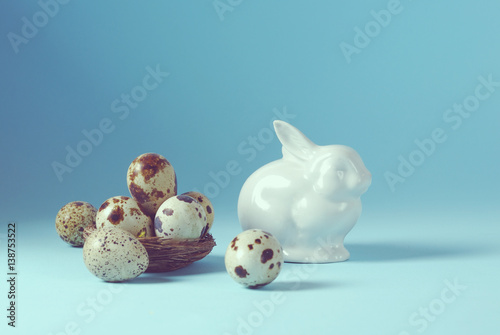 Easter holiday still life background with white porcelain bunny and quail eggs in the nest