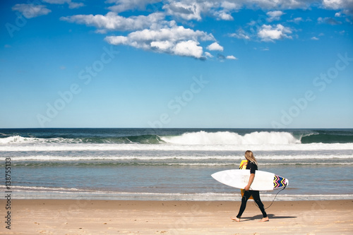 surfer walk along the shore of byron bay beach, NSW Australia.