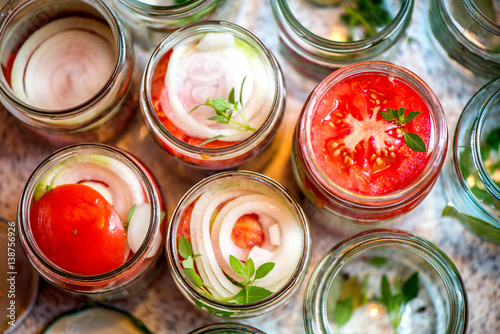 Canning fresh tomatoes with onions for winter in jelly marinade. A shot of basil leaves on top of a red ripe tomato slices and onion rings being put in jar.