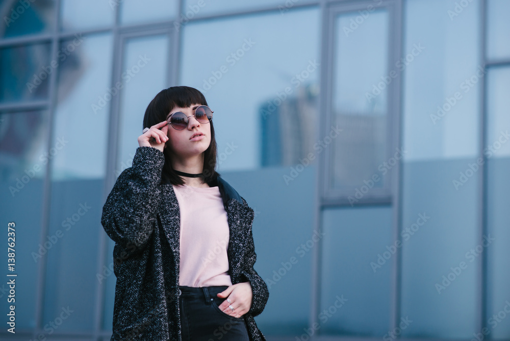 portrait of a young, beautiful and stylish dressed girl in the spring which adjusts his glasses and posing on urban background portrait of a young, beautiful and stylish dressed girl in the spring which adjusts his glasses and posing on urban background