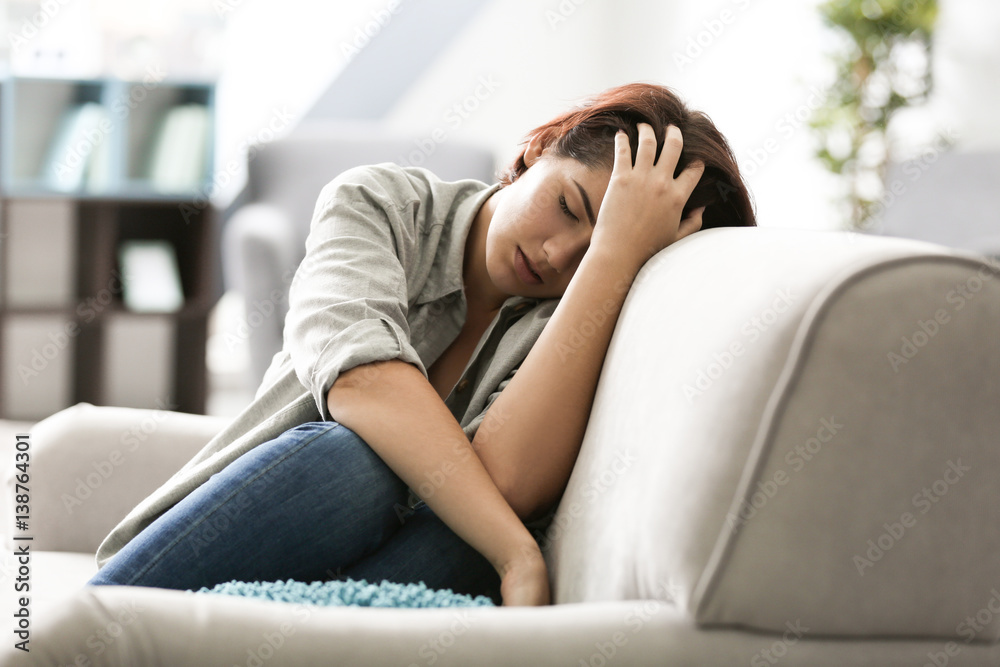 Depressed young woman sitting on sofa at home Depressed young woman sitting on sofa at home