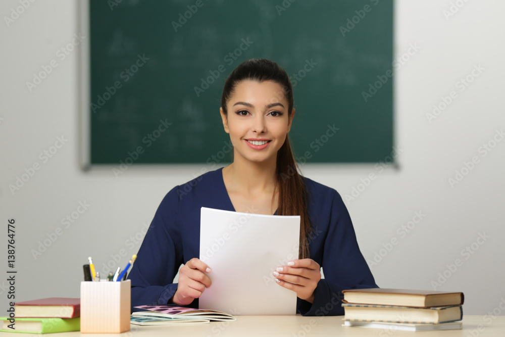 Beautiful young teacher sitting at table in classroom Beautiful young teacher sitting at table in classroom