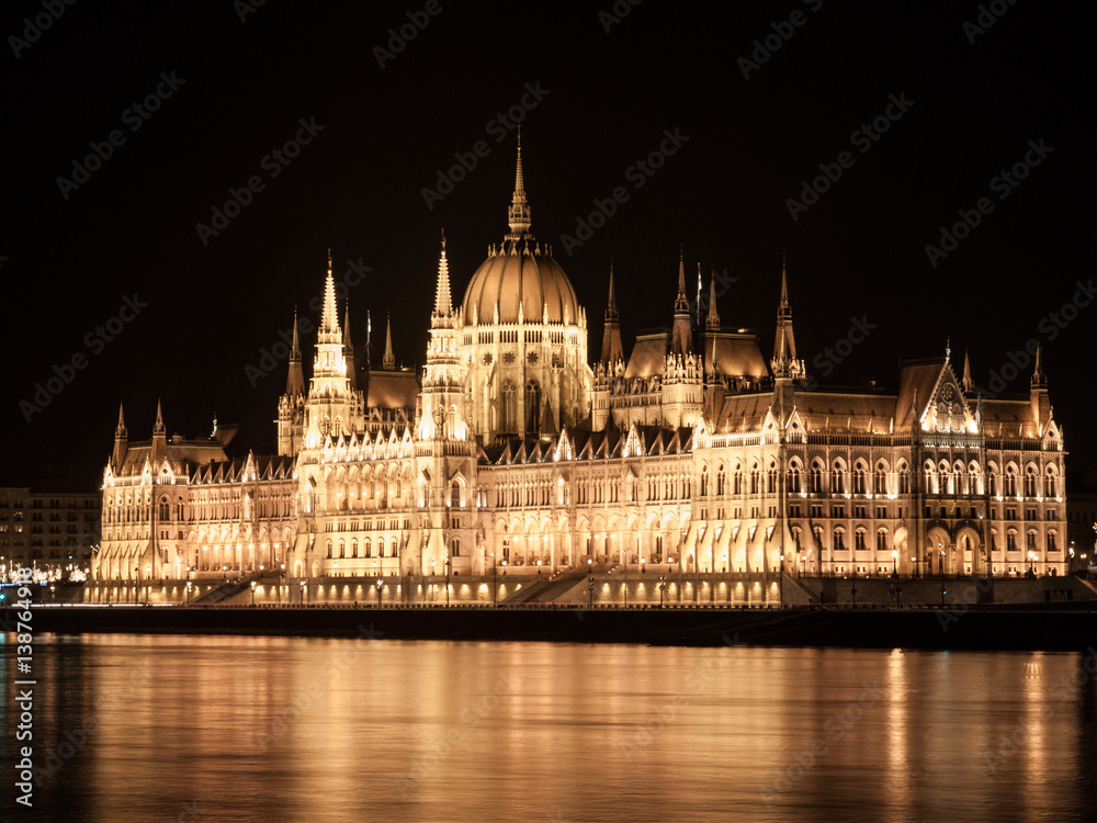 Night view of illuminated historical building of Hungarian Parliament, aka Orszaghaz, with typical symmetrical architecture and central dome on Danube River embankment in Budapest, Hungary, Europe. It