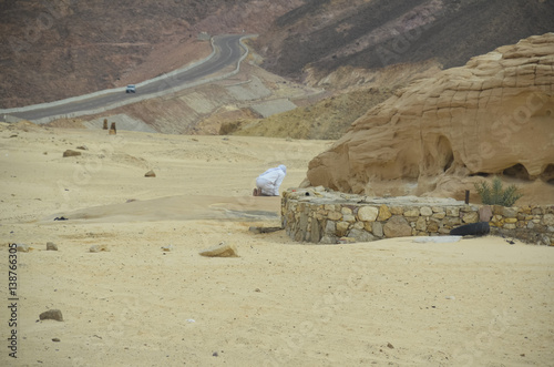 A man praying on his knees alone in the desert near the road