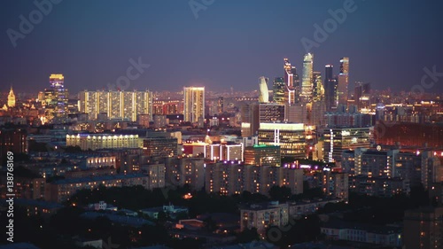 Time lapse tilt shift shooting from high above of evening and nightfall in big modern city with many lights turning on, clear sky, business skyscrapers in distance, residential houses in foreground
