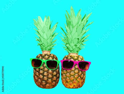 Two pineapple with sunglasses on blue background, colorful ananas photo