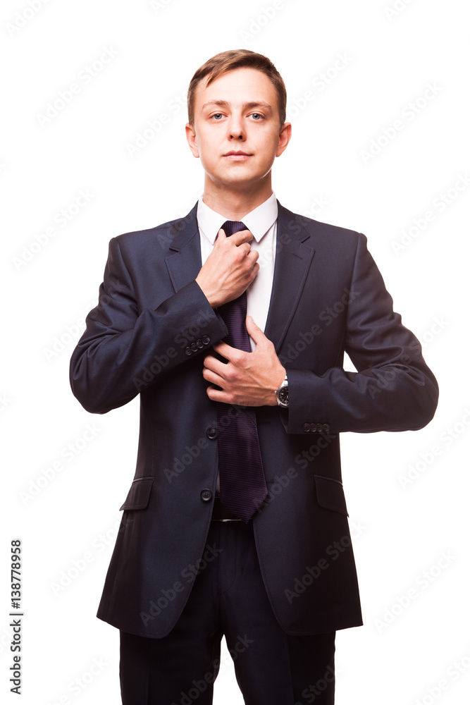 Stylish young man in suit and tie. Business style. Handsome man is standing, looking at the camera and fixing his tie Stylish young man in suit and tie. Business style. Handsome man is standing, looking at the camera and fixing his tie