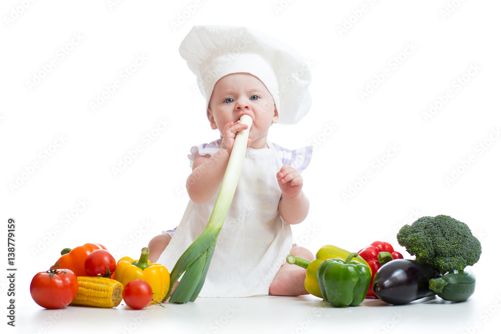 Little girl dressed in white chef hat and apron eats fresh onion. Child with vegetables: eggplant, popcorn, broccolli, peppers, zucchini, tomatoes Little girl dressed in white chef hat and apron eats fresh onion. Child with vegetables: eggplant, popcorn, broccolli, peppers, zucchini, tomatoes