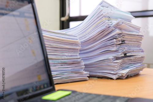 computer notebook and documents on desk stack up high waiting to be managed