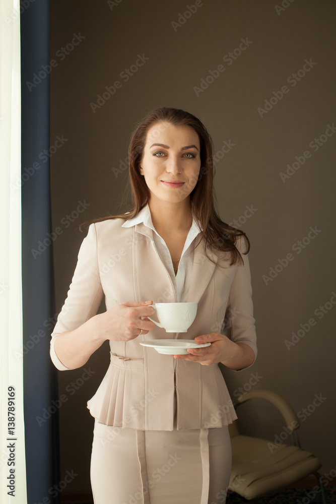 Businesswoman with tea cup looking through office window Businesswoman with tea cup looking through office window