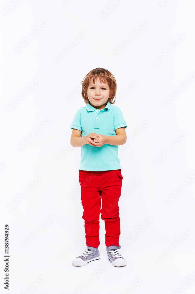 Full body shot of shy little boy dressed in bright colorful clothes standing smiling and twiddling hands against white background Full body shot of shy little boy dressed in bright colorful clothes standing smiling and twiddling hands against white background
