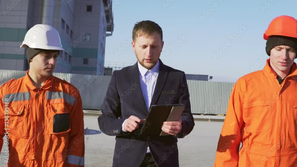 Engineer in a suit and two workers in orange uniform and helmets are ...