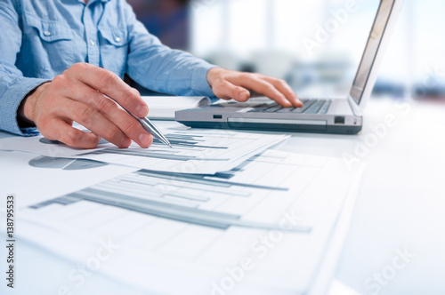 business documents on office table with smart phone, laptop computer and businessman enters data in the background