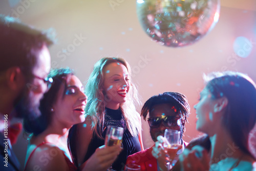 Dressy multiethnic group of friends gathered together and celebrating momentous event in nightclub, they laughing and drinking alcohol